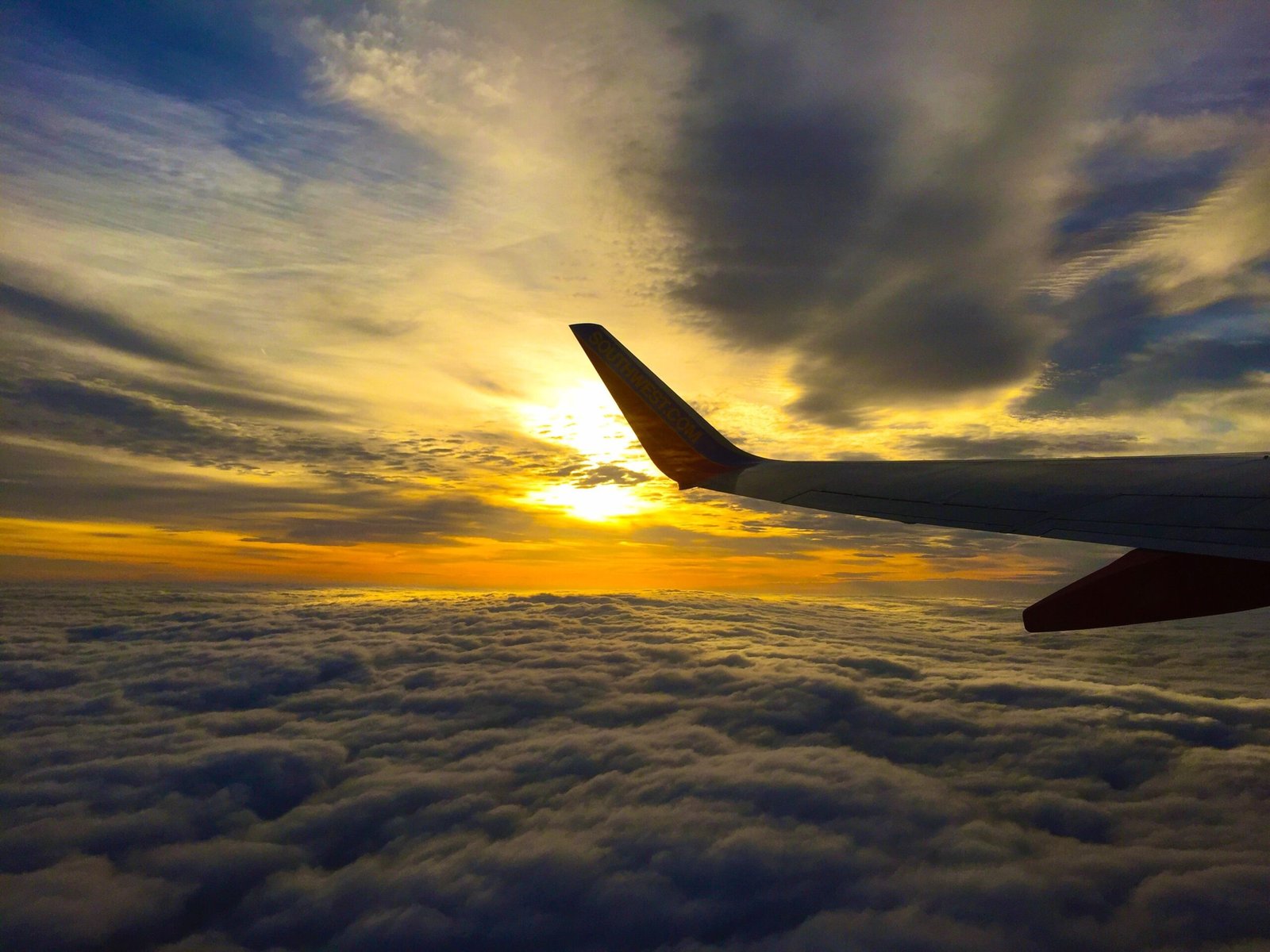 Airplane wing above clouds at sunset